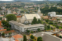 Foto tirada de cima de um prédio na Rua Curitibanos, mostrando a parte alta do Centro de Caçador e bairros ao fundo. Se destaca a Catedral São Francisco de Assis. Foto 2006